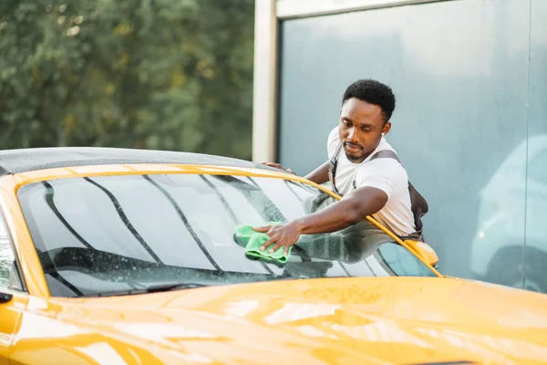 Yakışıklı sakallı genç adam spor arabanın ön camını temizliyor. — Stok fotoğraf