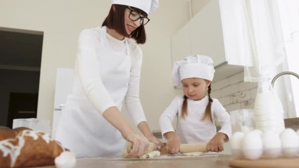 Cerca de la madre enseñando a la pequeña hija a trabajar con el rodillo de pie en la mesa en la cocina. — Vídeo de stock