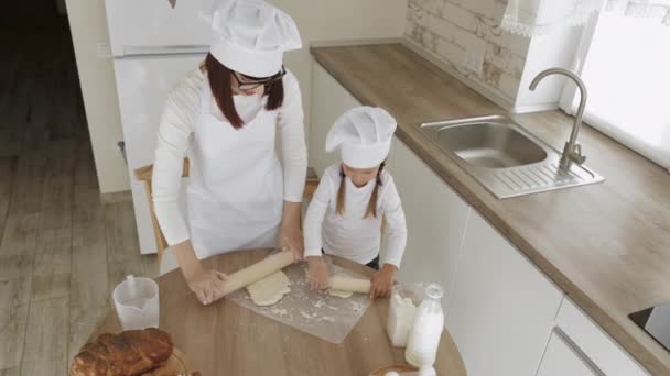 Caucasian mother and her beloved little daughter using two wooden rolling pins to roll the dough — Stock Video