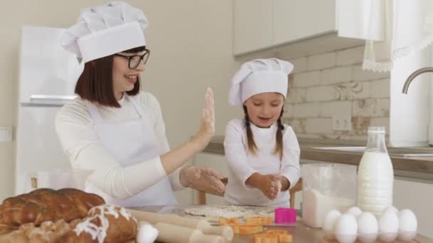 Mãe branca e filha adorável em chapéus de chef e avental branco gostando de cozinhar juntos — Vídeo de Stock