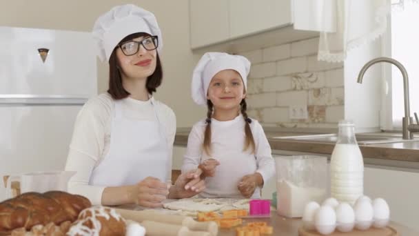 Menina branca feliz bonito e sua mãe em chapéus brancos de chef e aventais com farinha em rostos — Vídeo de Stock