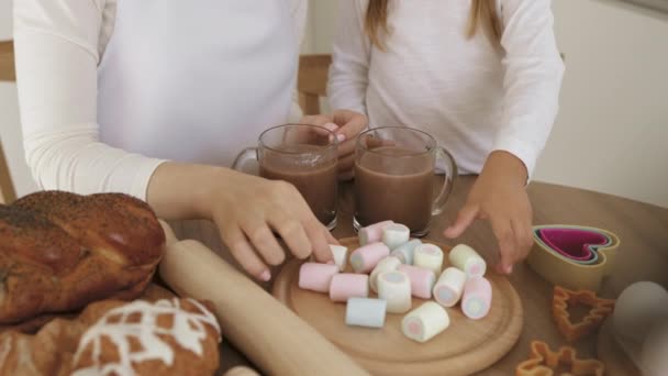 Close-up zicht op de handen van een vrouw en haar dochter die marshmallows in een glas cacao stoppen — Stockvideo