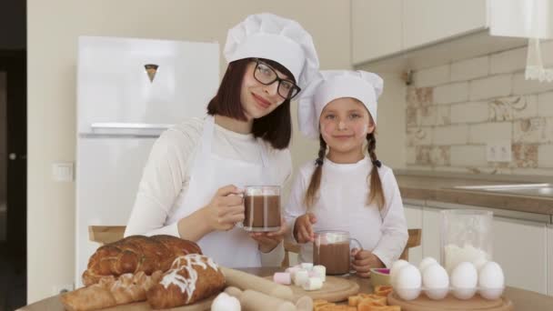 Linda chica y su mamá con caras untadas con harina bebiendo cacao caliente con malvavisco — Vídeo de stock