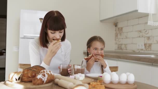 Ragazza carina e sua madre con i volti spalmati di farina stanno mangiando croissant e bevendo cacao — Video Stock