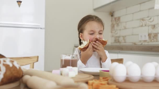Biała dziewczyna je rogaliki i pije kakao z piankami w domu w kuchni — Wideo stockowe