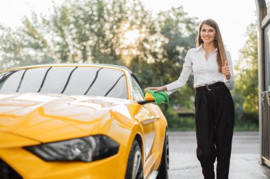 Beyaz gömlekli ve siyah pantolonlu bir iş kadını dikiz aynasını siliyor.