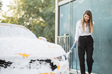 Çekici beyaz kadın iş yerinde giyinmiş. Sarı arabasını köpükle yıkıyor.