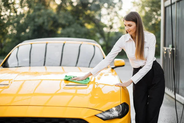 Smiling young caucasian businesswoman on white shirt and black pant, cleaning modern sport car hood — Stok Foto