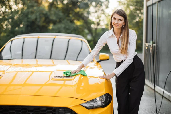 Wanita muda Kaukasia dalam pakaian bisnis kemeja putih dan celana hitam menyeka mobil kuning — Stok Foto