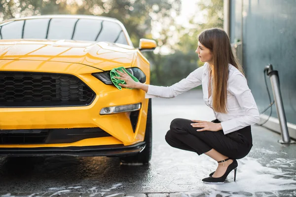 Wanita bisnis yang ceria mencuci dan menyeka modern olahraga mobil kuning lampu depan — Stok Foto