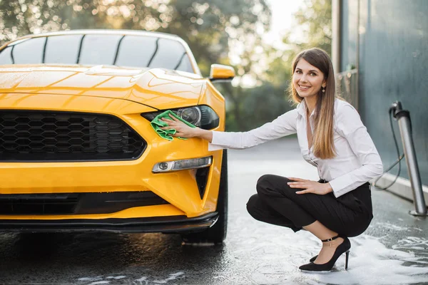 Wanita bisnis yang ceria mencuci dan menyeka modern olahraga mobil kuning lampu depan — Stok Foto