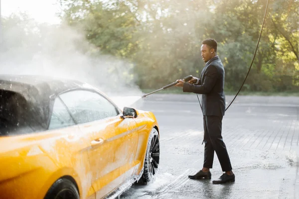 穿着西装、衣着时髦的非洲年轻人正在洗他的现代跑车 — 图库照片