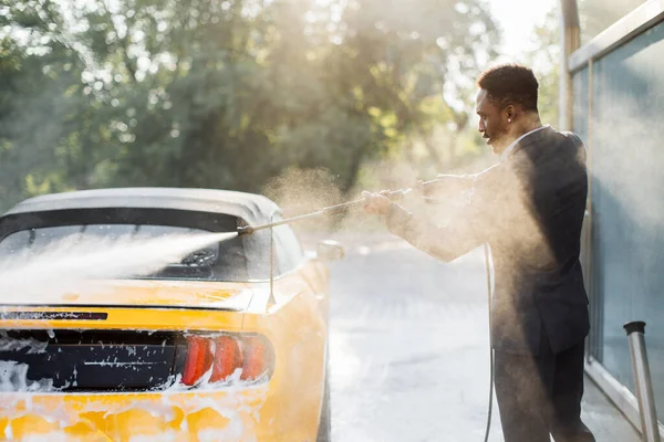 Resmi olarak Afrikalı Amerikalı işadamı lüks sarı arabasının arkasını yıkıyor. — Stok fotoğraf