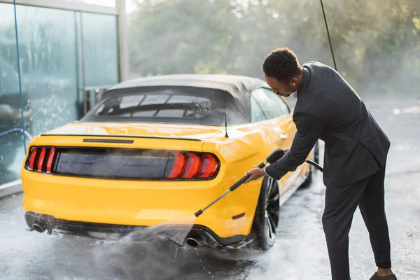 Girişimci takım elbiseli, sarı arabasının arkasını elle yıkıyor. — Stok fotoğraf