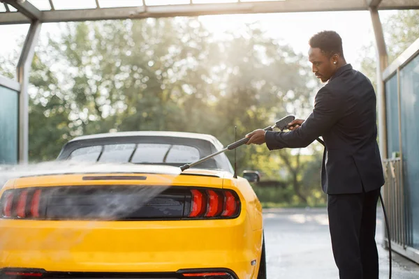 Підприємець у діловому костюмі, миття його жовтого автомобіля вручну — стокове фото