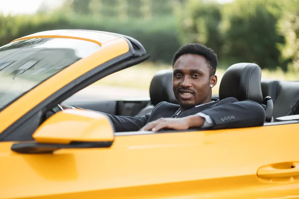 수염을 기른 젊은 아프리카 사업가가 노란 자동차를 운전하며 행복하게 웃고 있다 — 스톡 사진