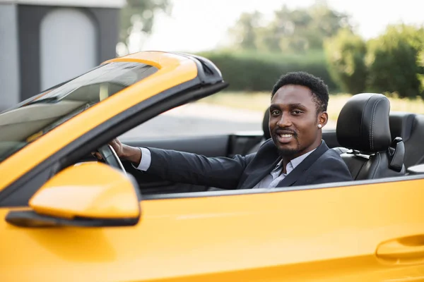 아프리카 계 미국인잘생긴 남성 럭셔리 스포츠 차량에 앉아서 옆을 바라보며 웃고 있는 모습 — 스톡 사진