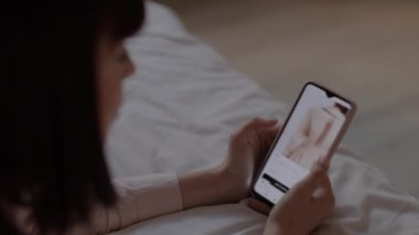 Çevrimiçi mağazada akıllı telefondan elbise arayan bir kadın..