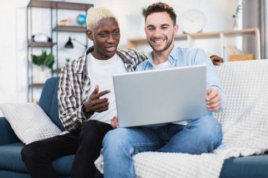 Koltukta dizüstü bilgisayar kullanan çok ırklı ve aynı cinsiyetten bir çift.