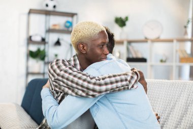 Konforlu koltukta kucaklaşan çok ırklı eşcinsel çift.