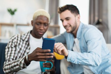 İki eşcinsel çay içiyor ve kanepede akıllı telefon kullanıyor.