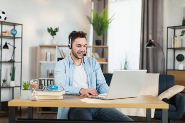 Kulaklık takmış bir adam modern laptopta video konferansı yapıyor.