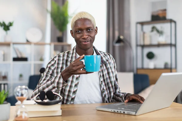 African american young sitting at desk with tea and laptop