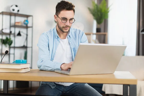 Άνθρωπος με γυαλιά κάθεται στο γραφείο και εργάζεται σε φορητό υπολογιστή — Φωτογραφία Αρχείου