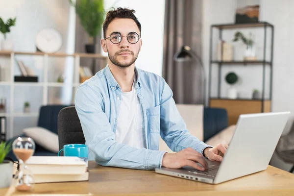 Όμορφος άντρας με γυαλιά που κάθεται στο γραφείο με φορητό υπολογιστή — Φωτογραφία Αρχείου