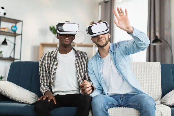VR kulaklıklı çok kültürlü eşcinsel çift kanepede oturuyor.