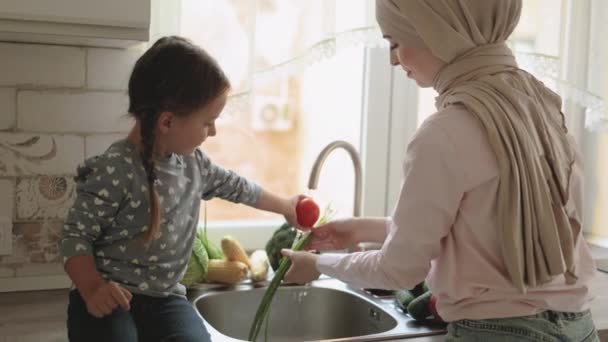 Vacker muslimsk kvinna med sin fyraåriga dotter tvättar grönsaker i diskhon — Stockvideo