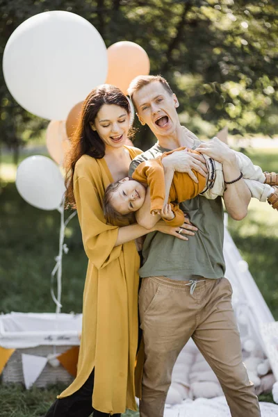 Família caucasiana de três brincando perto de wigwam ao ar livre — Fotografia de Stock