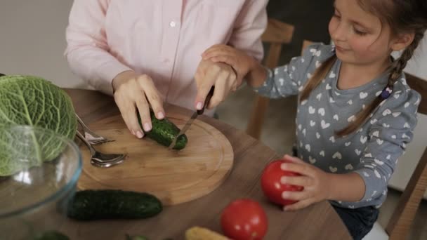 かわいい女の子と彼女のお母さんは野菜を切り、家で台所で調理しながら笑顔. — ストック動画