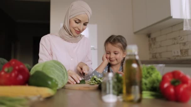 若いアラビア人の母親は小さな未就学児の娘を教える一緒に昼食のためのサラダを準備野菜を切る — ストック動画
