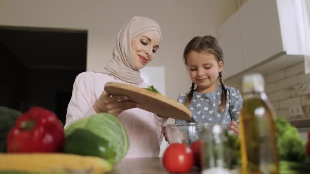 Nette Tochter bereitet Mittagessen mit muslimischer Mutter zu und wirft geschnittene Gurken in Glasschale — Stockvideo