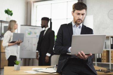 Takım elbiseli adam dizüstü bilgisayar kullanıyor ve toplantı odasına bakıyor.