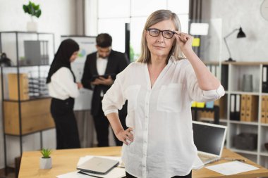 Modern ofiste poz veren kendinden emin, olgun bir kadın.