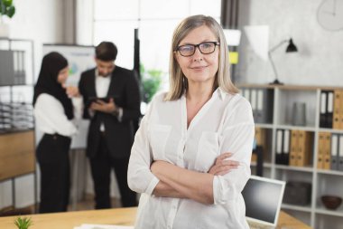 Ofiste kollarını kavuşturmuş beyaz saçlı beyaz kadın.