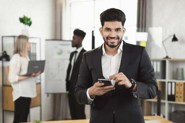 Homme d'affaires indien avec mobile souriant à la caméra au bureau — Photo