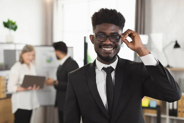 Homme africain souriant en costume et lunettes posant au bureau — Photo