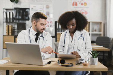 İki farklı doktor dizüstü bilgisayar ve kağıtlarla toplantı yapıyor.