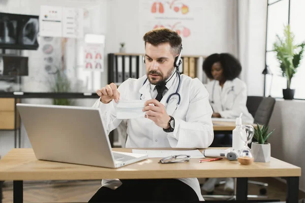 Yüz maskeli doktor video araması için dizüstü bilgisayar kullanıyor. — Stok fotoğraf