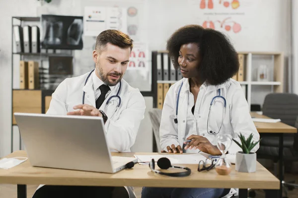 Çok ırklı tıp çalışanları masada dizüstü bilgisayarlarıyla oturuyorlar. — Stok fotoğraf