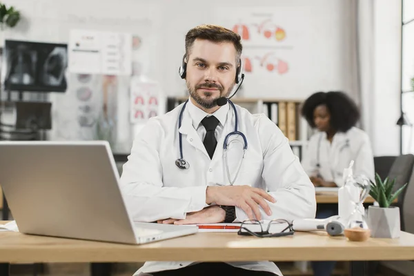 Доктор в наушниках с видеозвонком на ноутбуке — стоковое фото