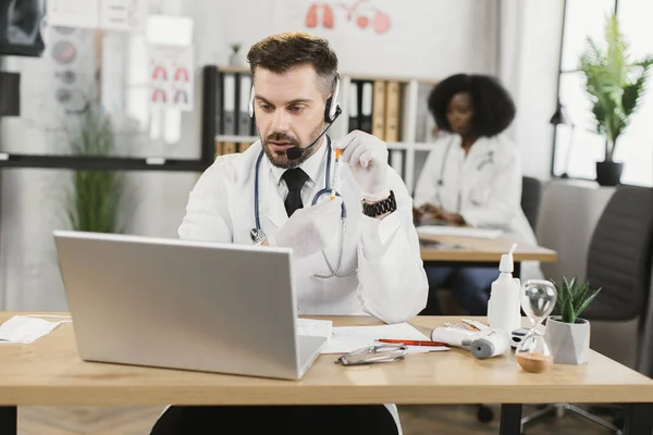 Medico che utilizza auricolari e laptop per la consultazione online — Foto Stock