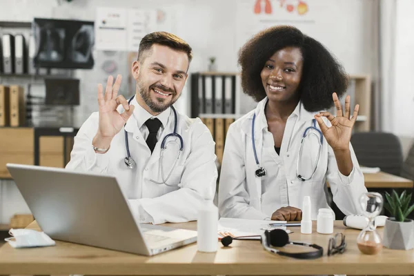 Multi etnico medici gesturing segno ok e sorridente sulla macchina fotografica — Foto Stock