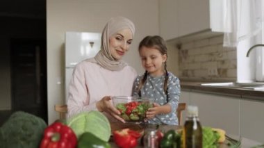 Sevimli küçük kız tesettürlü genç anneden yemek pişirmede ustalaşıyor.