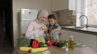 Arap kadın anne, Kafkasyalı küçük şirin kıza sağlıklı vejetaryen yemekleri yapmayı öğretiyor.