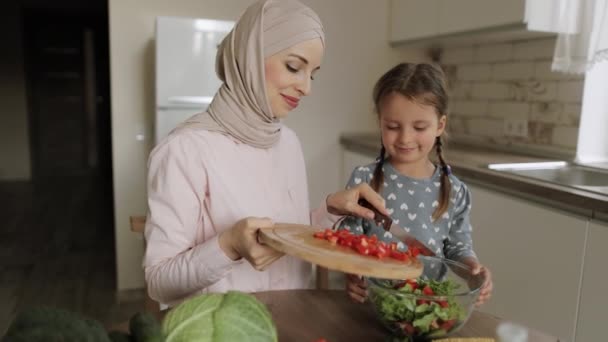 Linda hija preparar el almuerzo con mamá musulmana lanzando pimiento en rodajas en tazón de vidrio — Vídeos de Stock