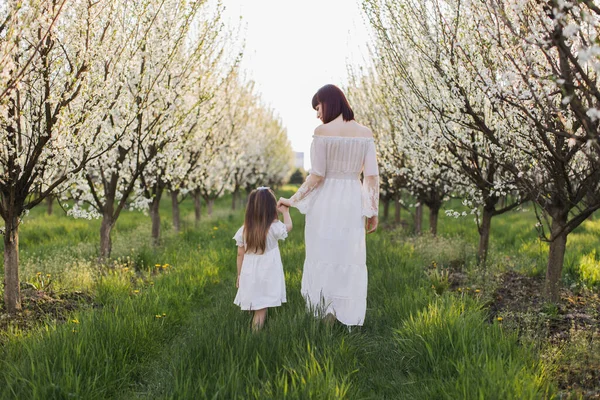 Mother with daughter holding hands and walking at garden